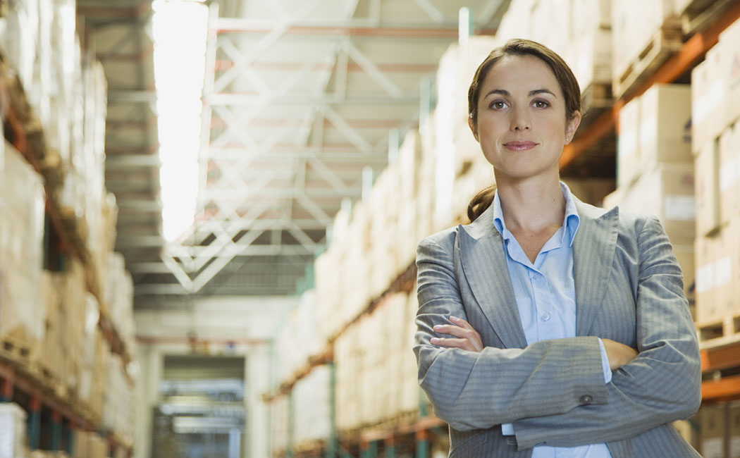 Female executive in blue shirt and jacket standing next to shelves in warehouse, Enterprise Applications | DXC Technology