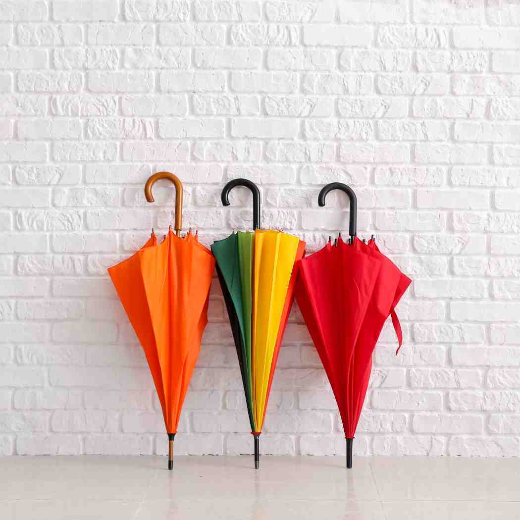 Three colorful umbrellas propped against a white brick wall, Insurance | DXC Technology Software